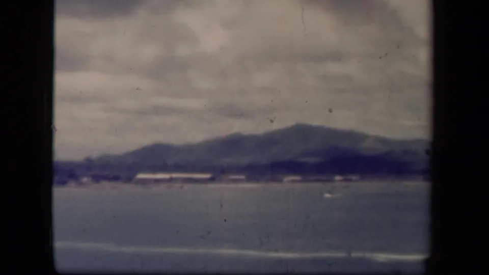 Leyte Gulf, Philippines, viewed from shore in 1944 home-movie footage, with overcast sky, distant mountains, calm water, and faint shore structures.