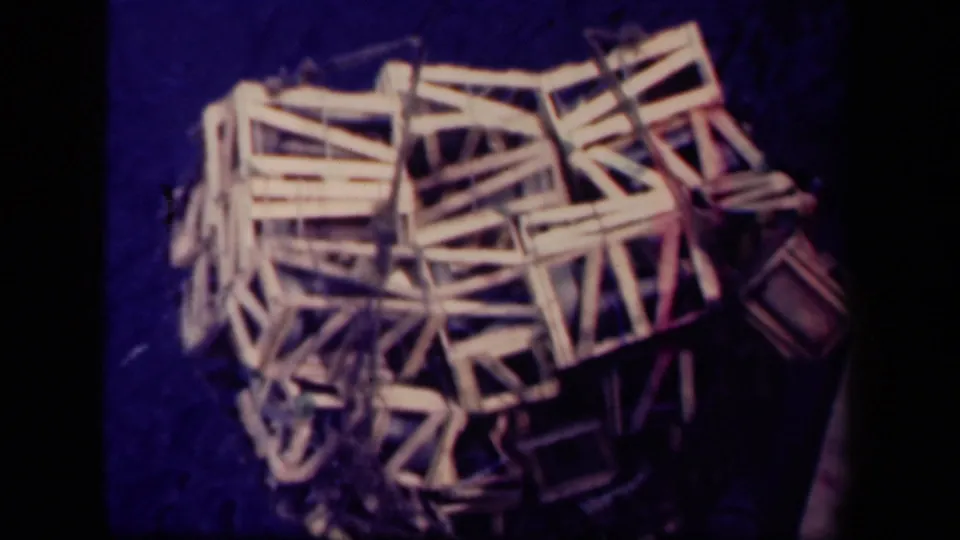 1944 Leyte Gulf 8mm frame showing a rope-suspended bundle of wooden crate frames against a dark blue shipboard or dockside surface.