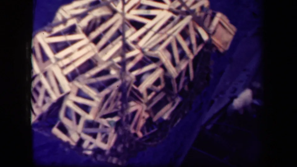 1944 Leyte Gulf 8mm frame showing a rope-held bundle of wooden crate frames beside a dark vertical surface, likely during cargo movement.