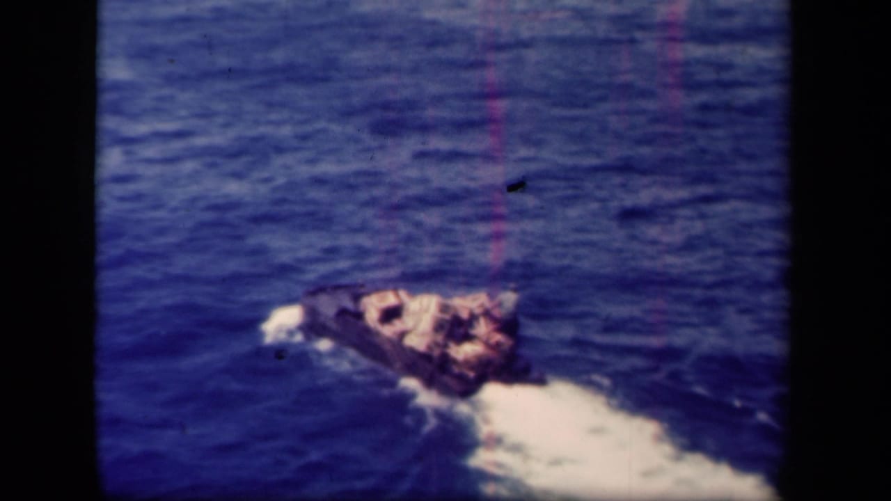 Leyte Gulf frame from 1944 showing the loaded boat farther from camera, surrounded by rippled blue water and wake.