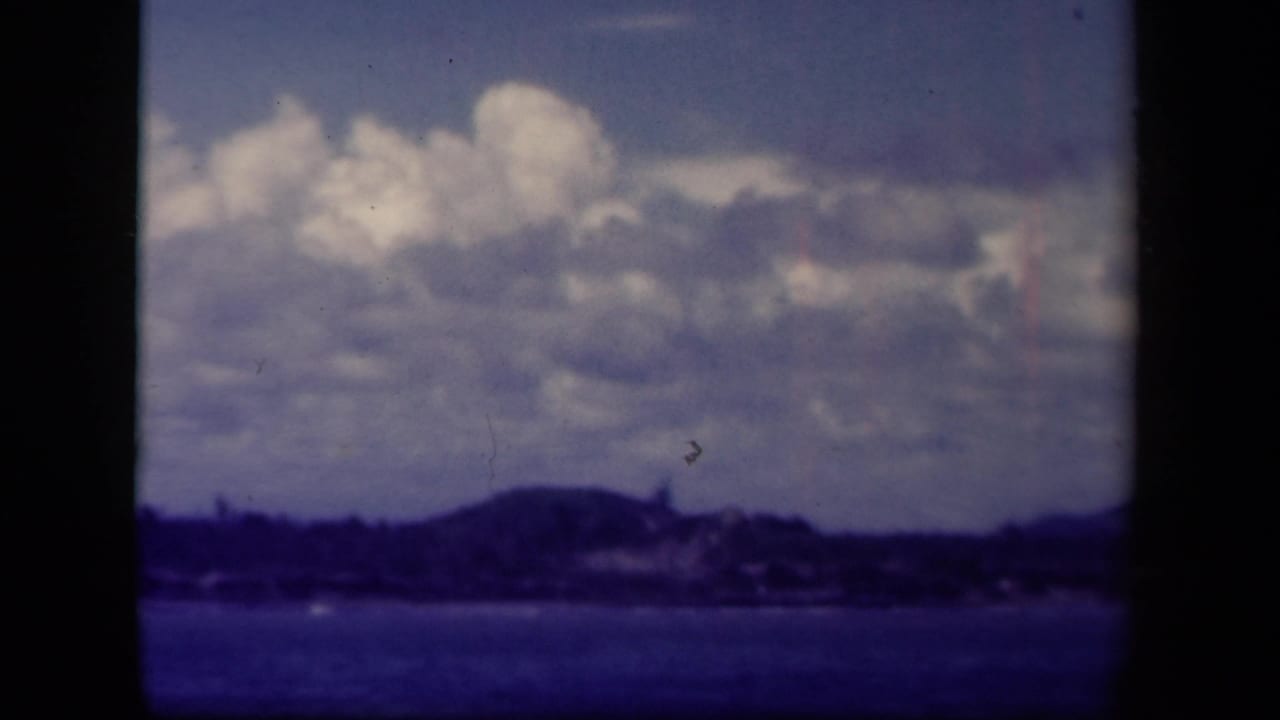 Soft distant shoreline and clouds across water, framed by black film borders.