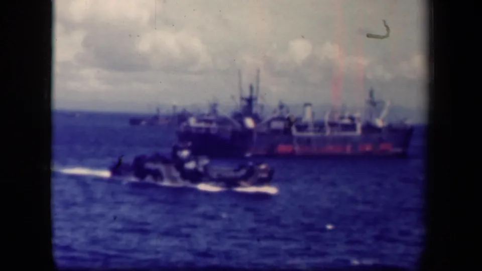 1944 Leyte Gulf 8mm view of a naval vessel at sea, with a smaller craft in front and cloudy horizon behind.