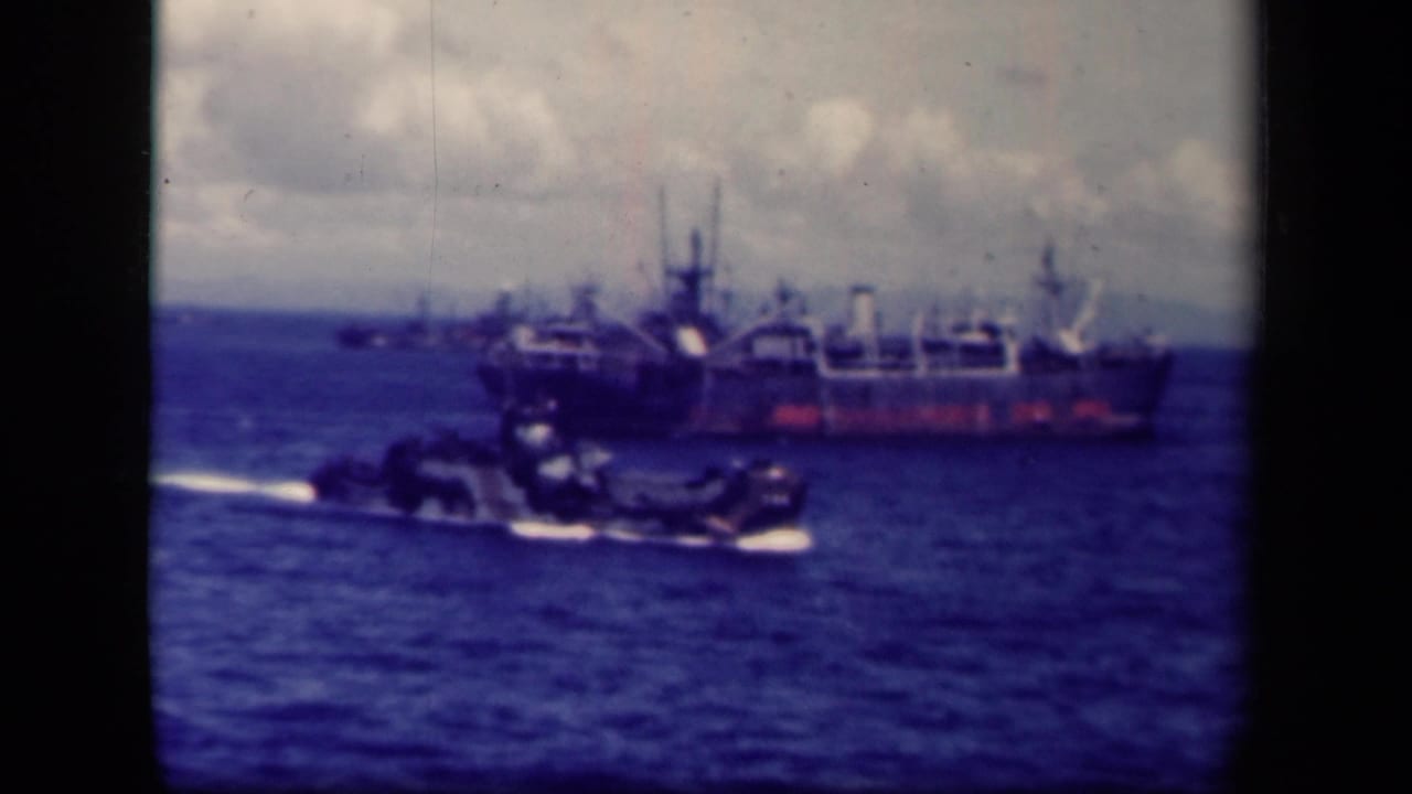 Large ship offshore with a small craft crossing in front on open water.