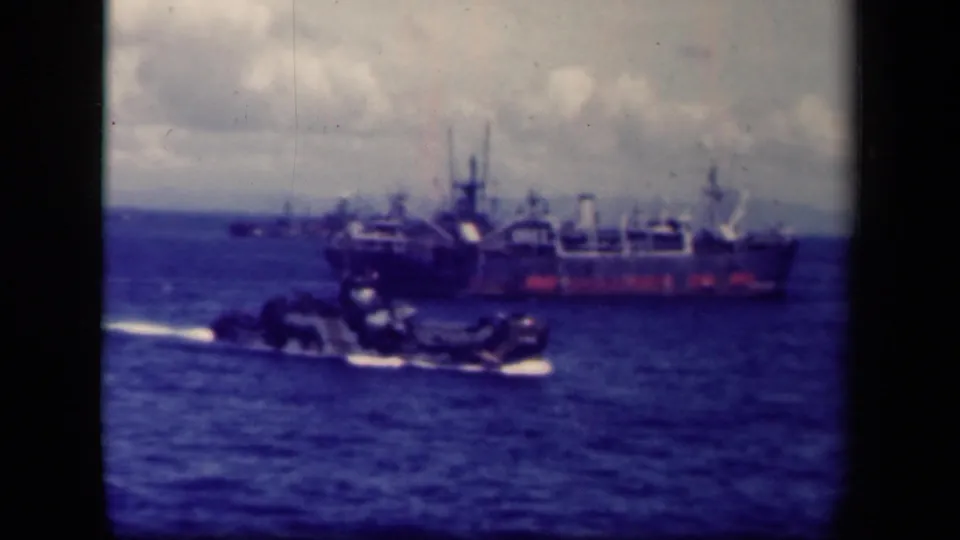 1944 Leyte Gulf view of a large cargo or support ship offshore with a smaller craft moving across the foreground.