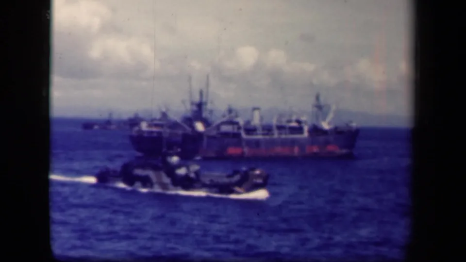 1944 Leyte Gulf shot of a small landing craft or boat on the sea, with a large ship anchored beyond it.
