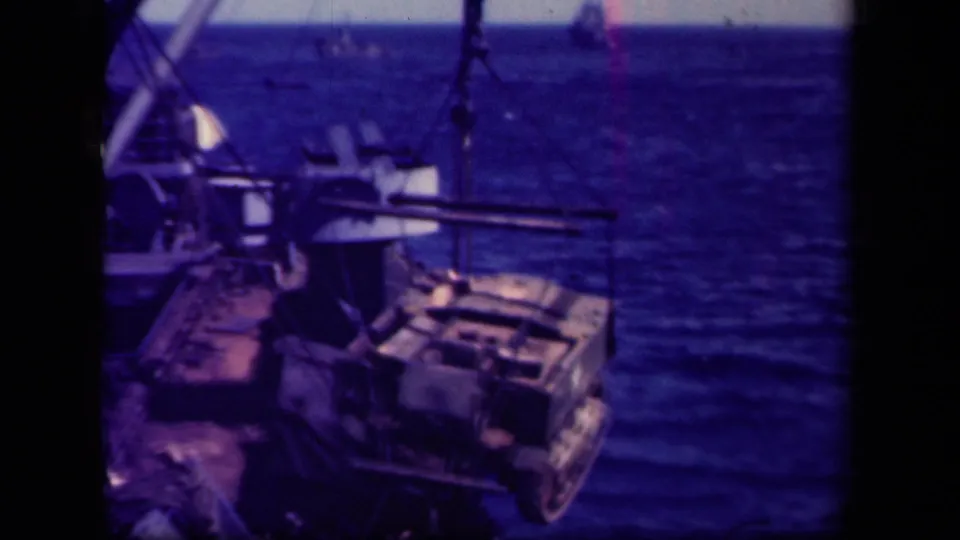 1944 Leyte Gulf shipboard view of a tracked military vehicle suspended by a crane above open water.