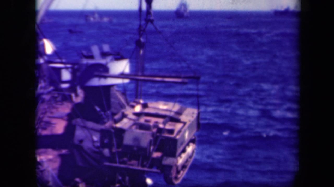 1944 Leyte Gulf shipboard view of a crane moving a large military load above the deck and ocean.
