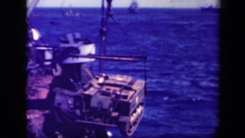1944 Leyte Gulf shipboard view of a crane moving a large military load above the deck and ocean.