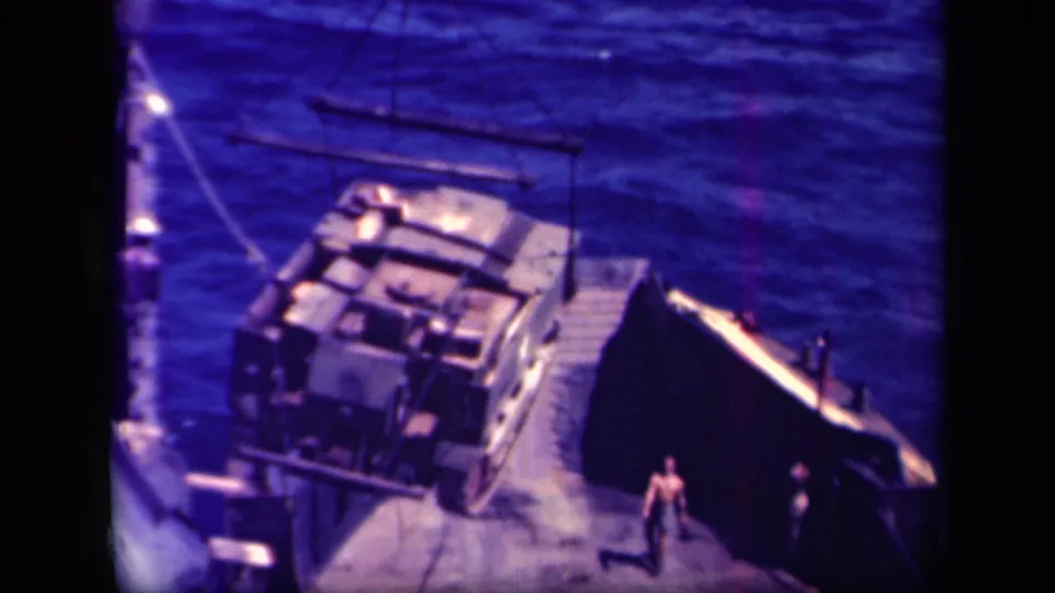 A crane positions a large military load near a ramp while a person stands on the deck in Leyte Gulf.