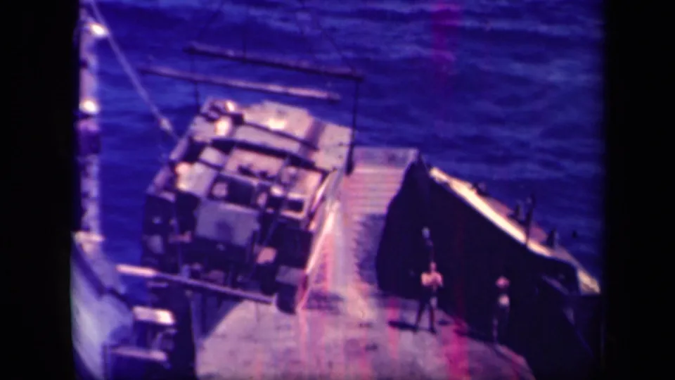 Two deck figures stand near a ramp as crane rigging holds a large load during the Leyte Gulf transfer.
