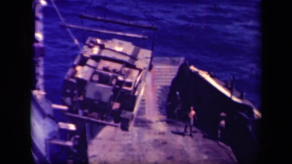 1944 Leyte Gulf home-movie frame showing a large military vehicle suspended by crane near a ship deck or dock edge.
