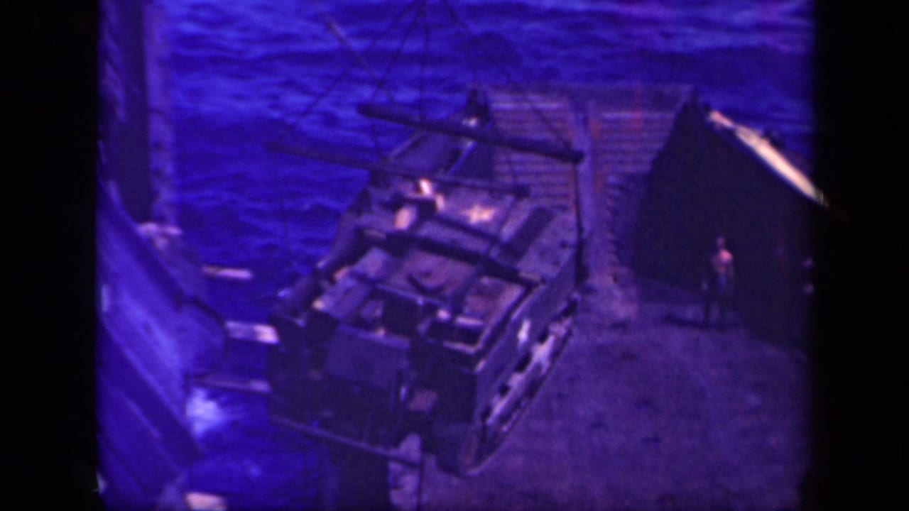 Overhead view of a vehicle hanging near a ship deck with choppy water behind it.