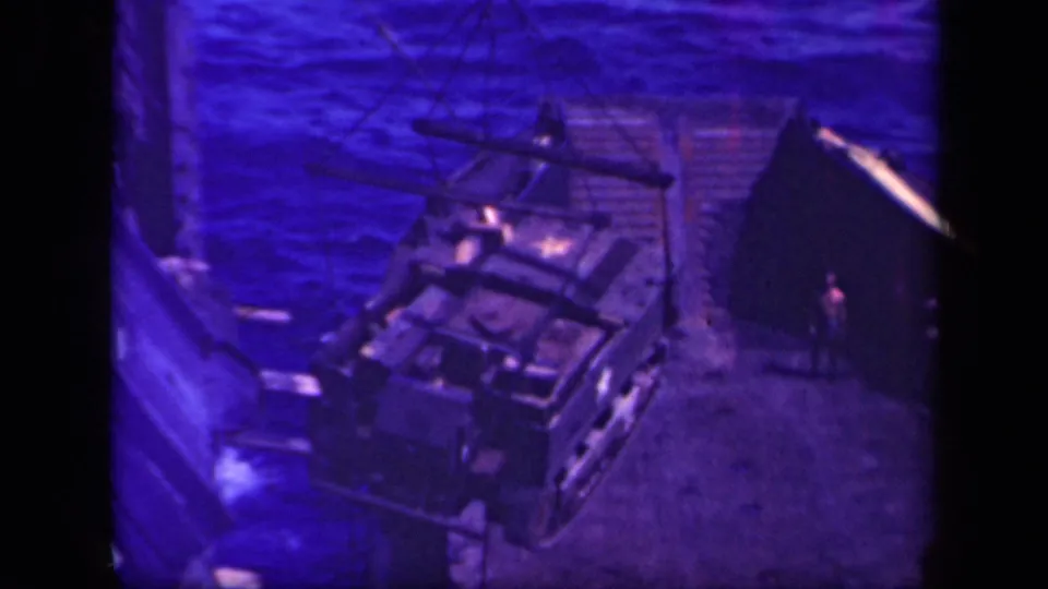 Overhead 8mm frame from Leyte Gulf showing a crane-lifted armored vehicle near a vessel or dock structure.