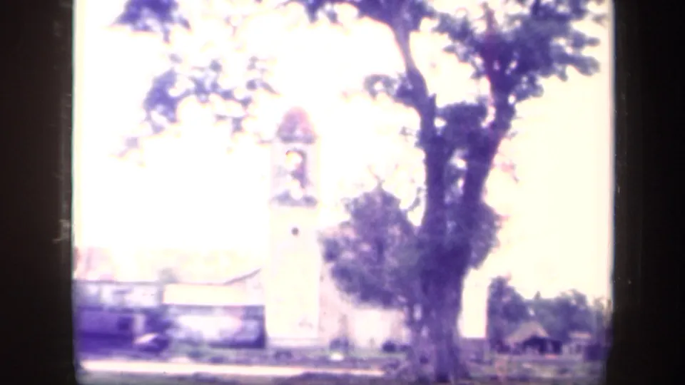 Brief Leyte Gulf area village view showing a white church tower, bell opening, wall, and large tree on aged 8mm film.