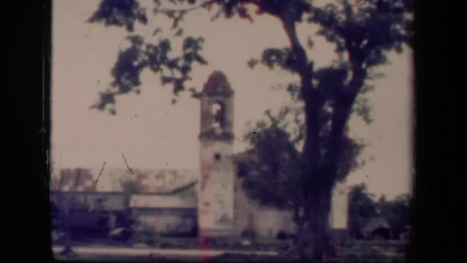 Tacloban frame from 1944 shows the church bell tower and a large tree dominating the view, with low damaged buildings behind them.