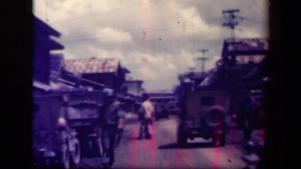1940s Leyte Gulf street scene with several men walking near parked vehicles, a cart, simple buildings, and utility poles.