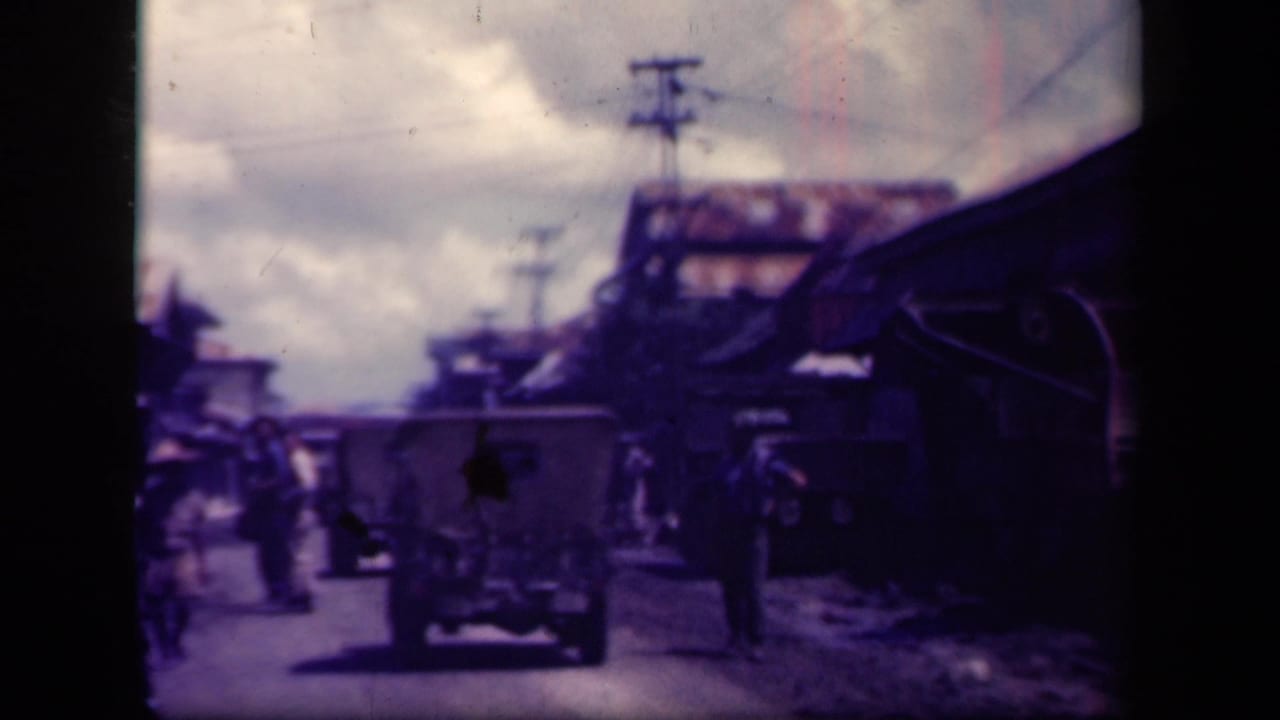 1944 Leyte Gulf footage shows vehicles and pedestrians on a dirt road with buildings and utility poles nearby.
