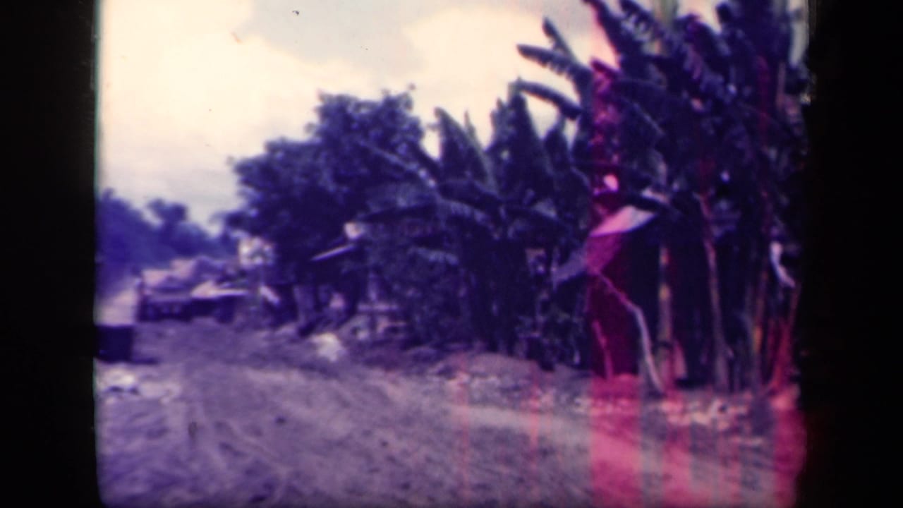 1944 Leyte Gulf 8mm frame showing a muddy village road, banana trees, and a distant vehicle or motorcycle shape.
