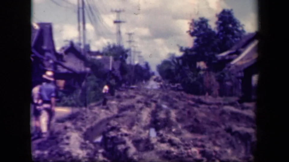 1944 Leyte Gulf street view showing a rutted muddy road, wooden roadside buildings, utility poles, and a person walking.