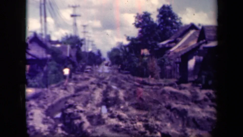 Leyte Gulf village road frame with deep mud ruts, roadside houses, trees, and utility poles receding into the distance.
