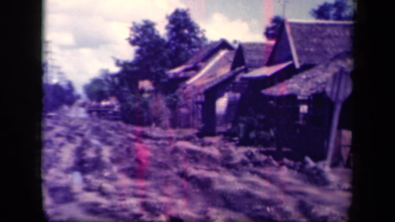 Muddy road and thatched houses with a truck farther down the village street.