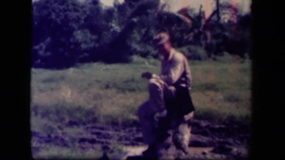 A man in military-style clothing sits on a stump in a grassy Leyte Gulf field during 1940s 8mm home-movie footage.