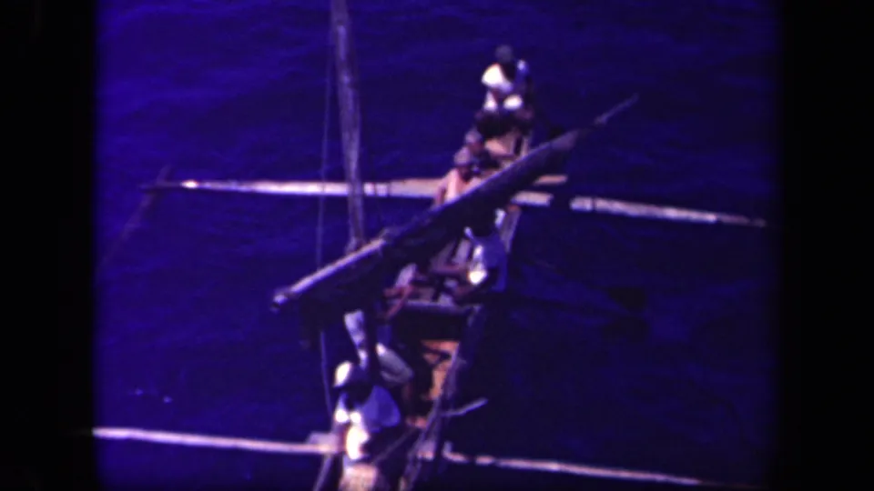 The outrigger canoe continues across dark blue water, with men seated along the hull and one figure near the stern.