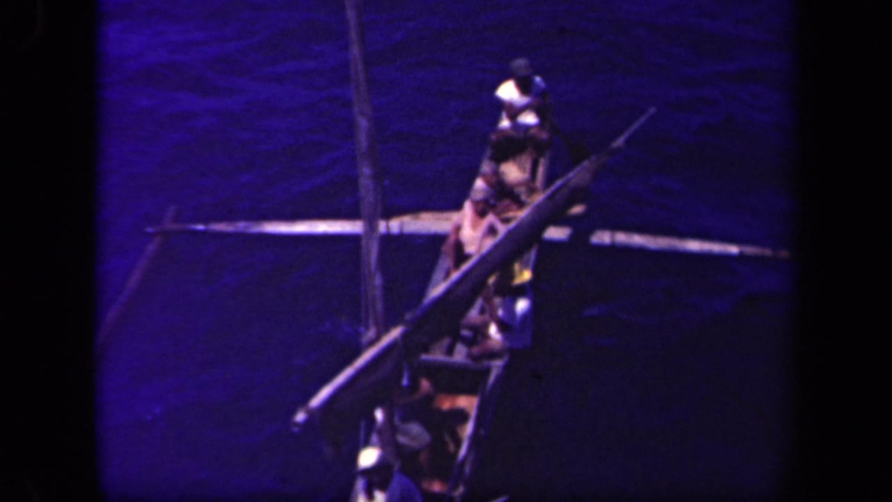 Overhead view of people aboard a narrow outrigger canoe on dark blue water.