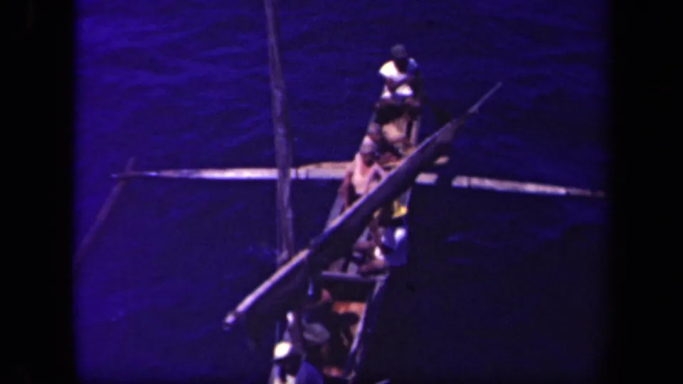 1944 Leyte Gulf footage showing several people in a traditional outrigger canoe, viewed from above across dark blue water.