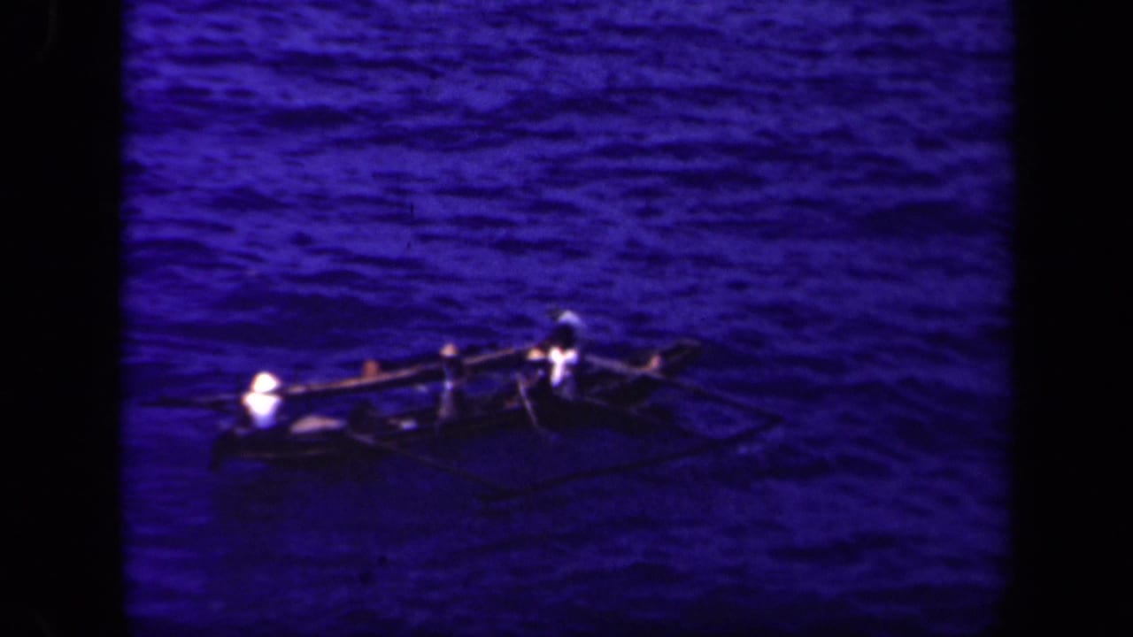 Small outrigger canoe with occupants crossing dark blue water.