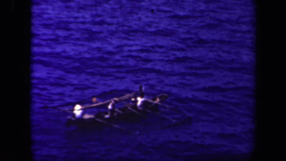 A distant outrigger canoe with several people aboard crosses rippled blue water in the 1944 Leyte Gulf home-movie clip.