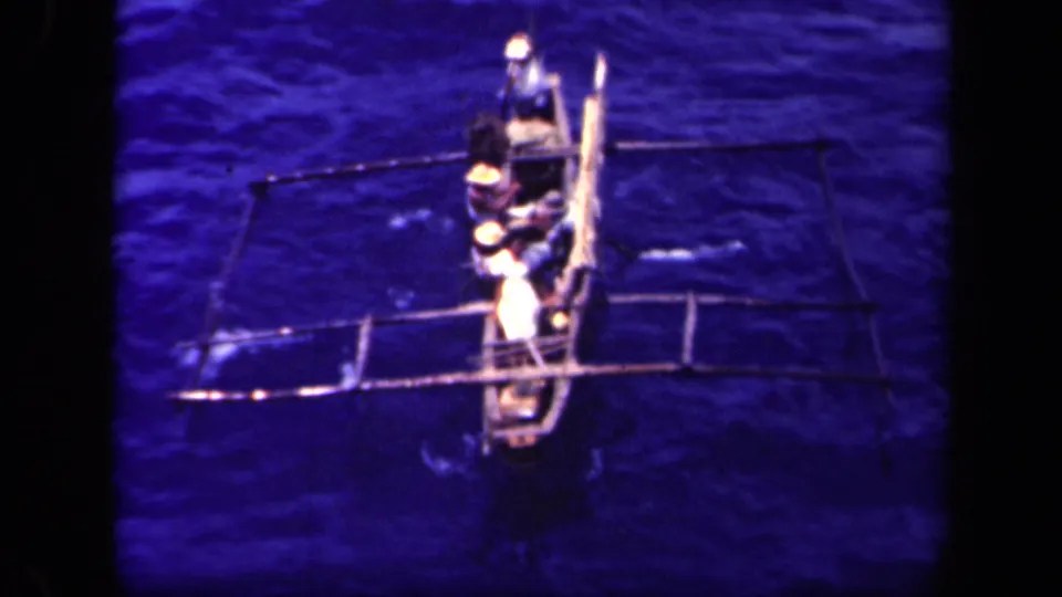 A closer overhead angle shows the outrigger canoe, multiple occupants, long supports, and paddles on blue water in Leyte Gulf.