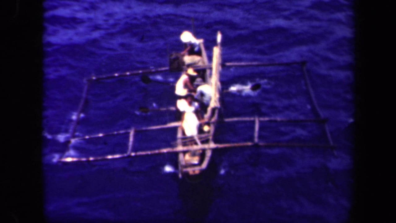 1944 Leyte Gulf footage shows several men in light clothing rowing a narrow outrigger canoe seen from above.