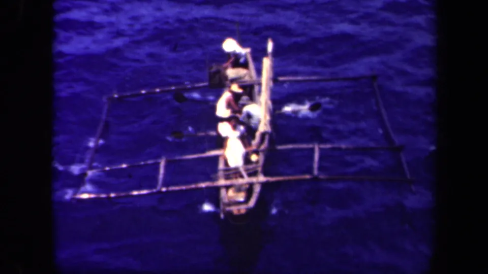 1944 Leyte Gulf footage shows several men in light clothing rowing a narrow outrigger canoe seen from above.