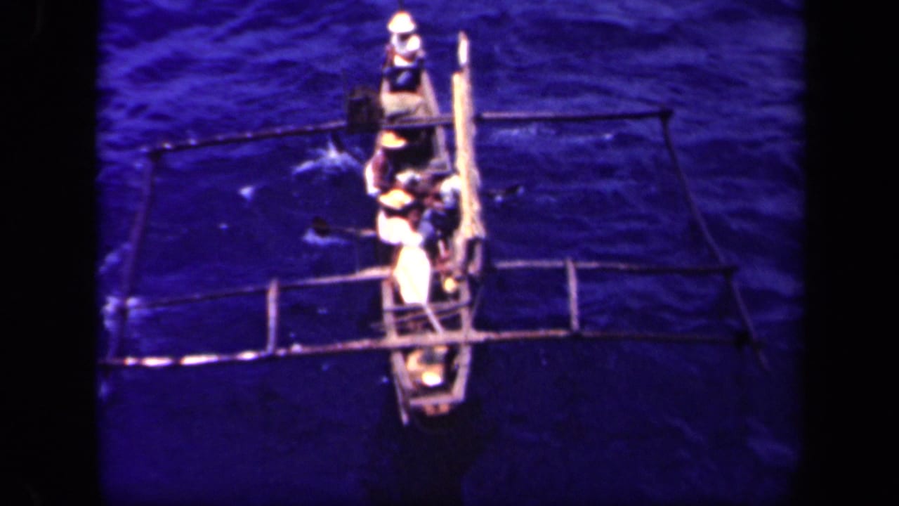 Several men continue rowing an outrigger canoe in Leyte Gulf, with paddles and side supports visible from a high angle.