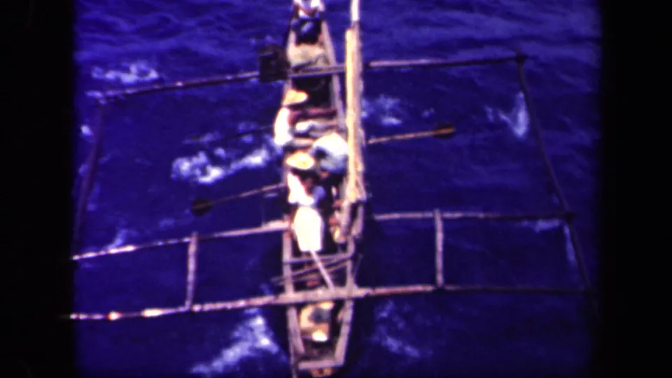 At the end of the clip, the canoe crew remains clustered around the narrow hull as paddles disturb the blue water.