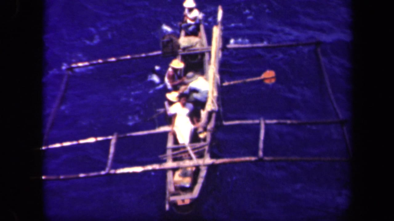 1944 Leyte Gulf footage shows several men in light clothing rowing a narrow outrigger canoe from a high angle.
