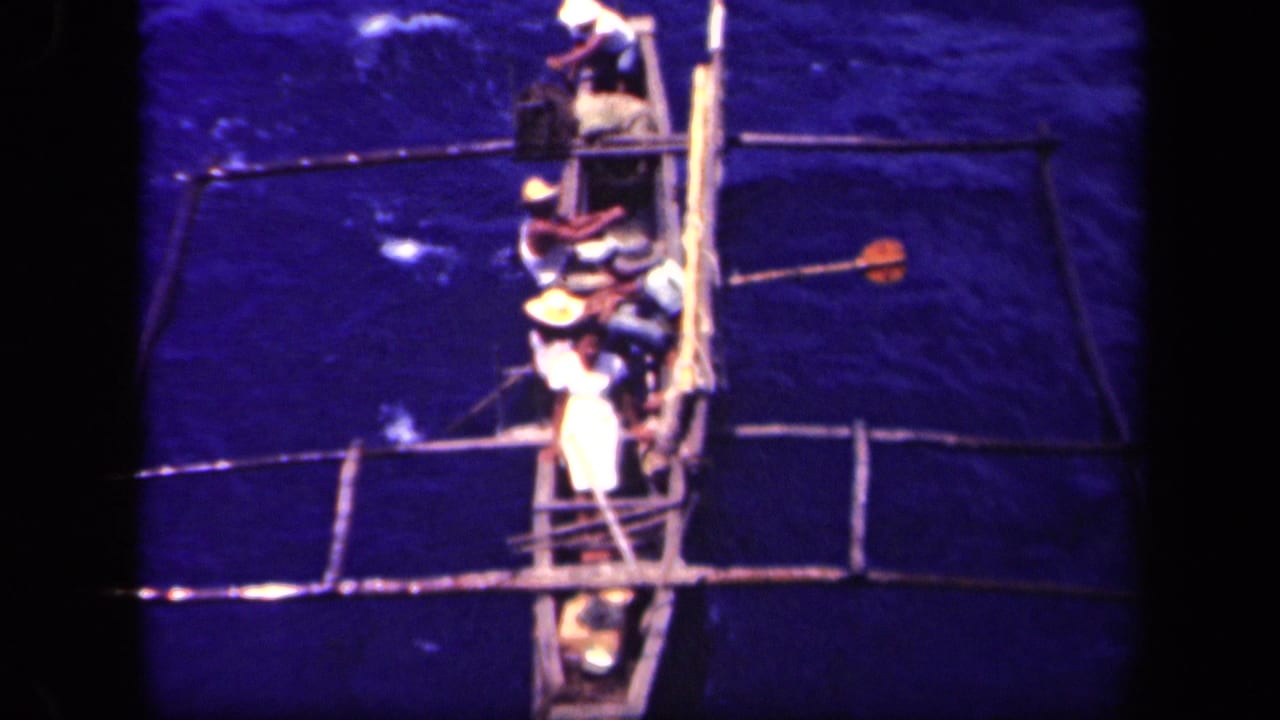 Outrigger canoe with rowers seen from above on open water.