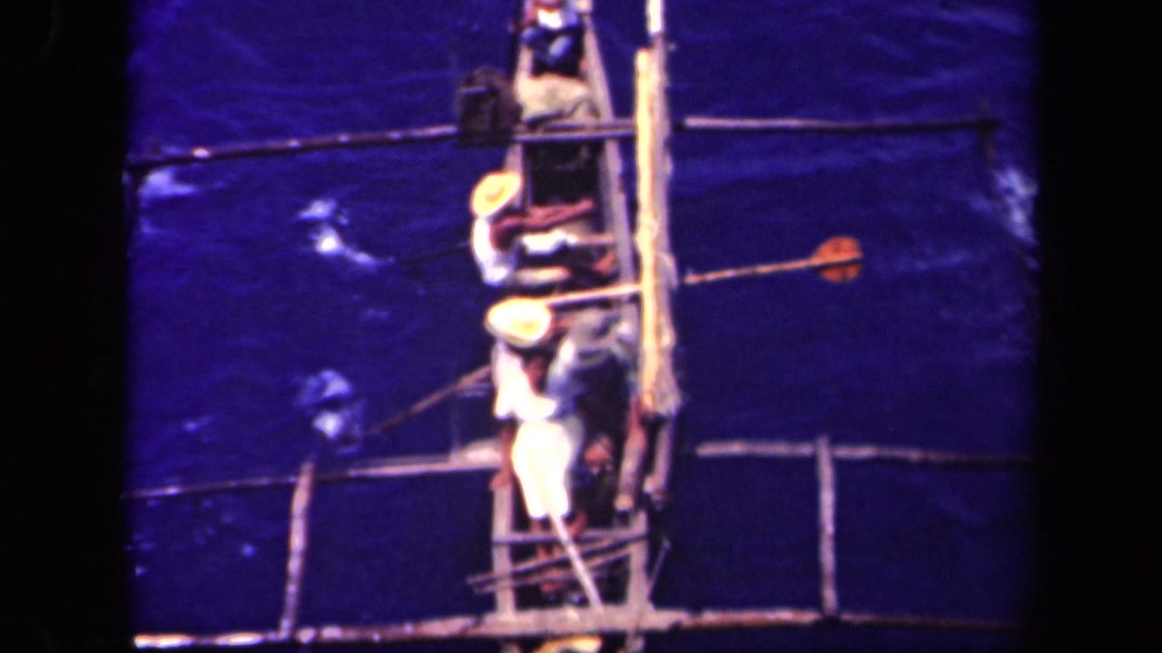 High-angle view of three men in a narrow wooden boat on dark blue water.