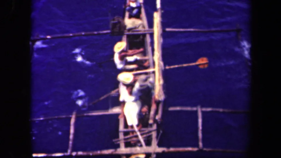 1944 Leyte Gulf 8mm frame showing three men from above in a narrow homemade boat with poles or oars on open water.