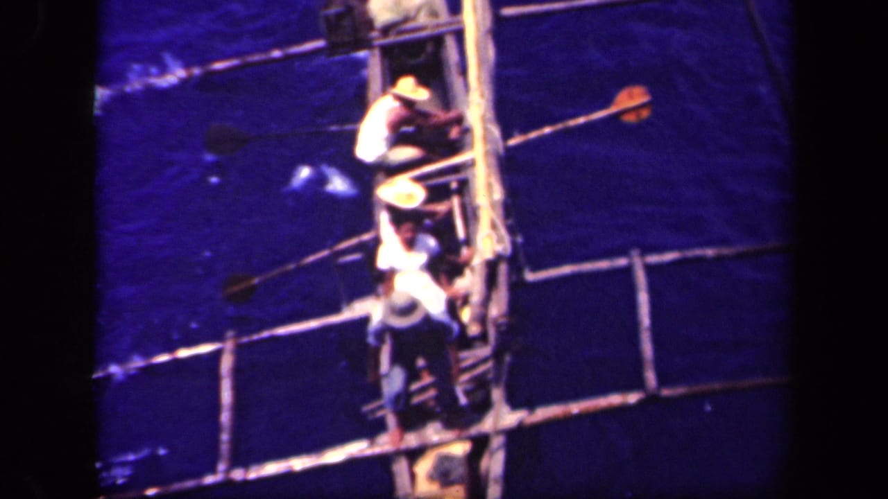 High-angle 8mm view in Leyte Gulf, Philippines, with men clustered on a small handmade boat and long poles crossing the frame.
