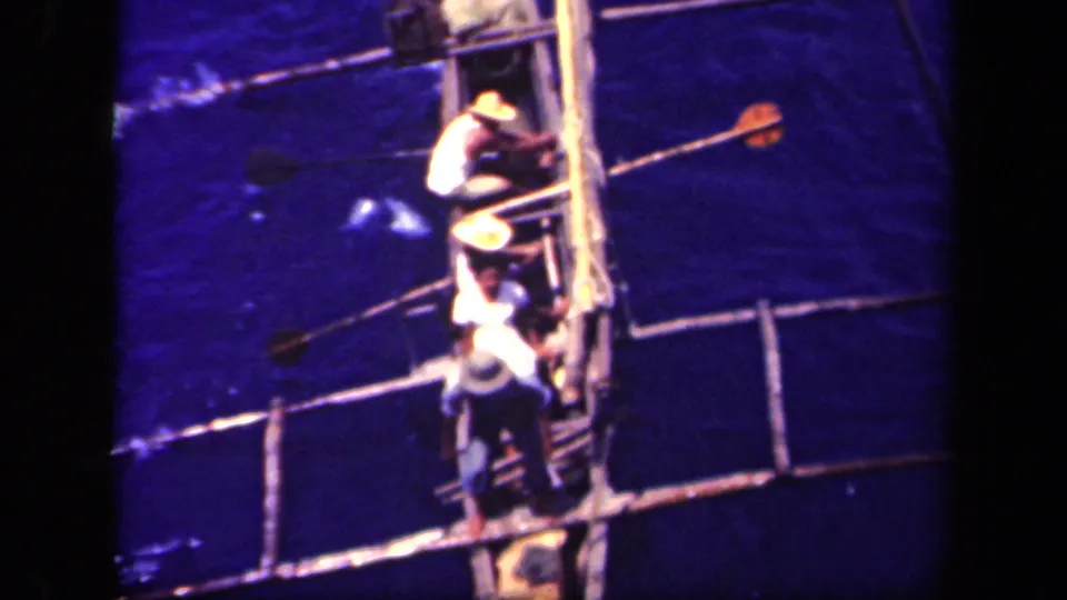 High-angle 8mm view in Leyte Gulf, Philippines, with men clustered on a small handmade boat and long poles crossing the frame.