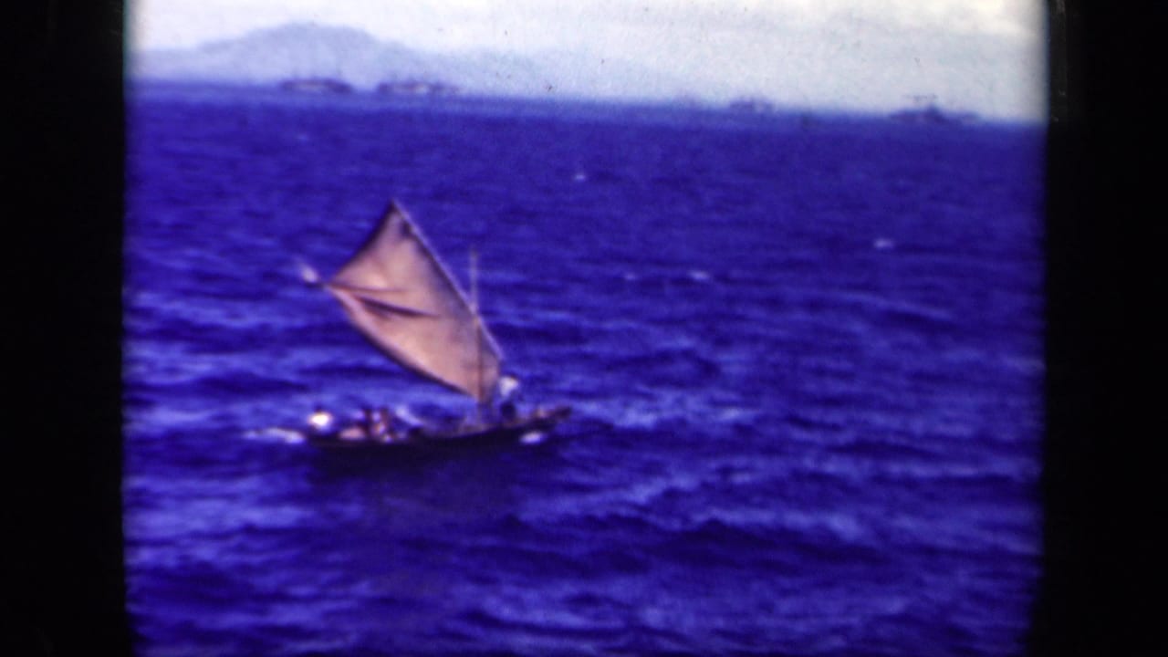 1944 Leyte Gulf 8mm frame showing a small crewed sailing vessel with a triangular sail on choppy blue sea.