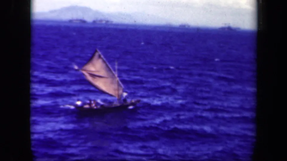 1944 Leyte Gulf 8mm frame showing a small crewed sailing vessel with a triangular sail on choppy blue sea.