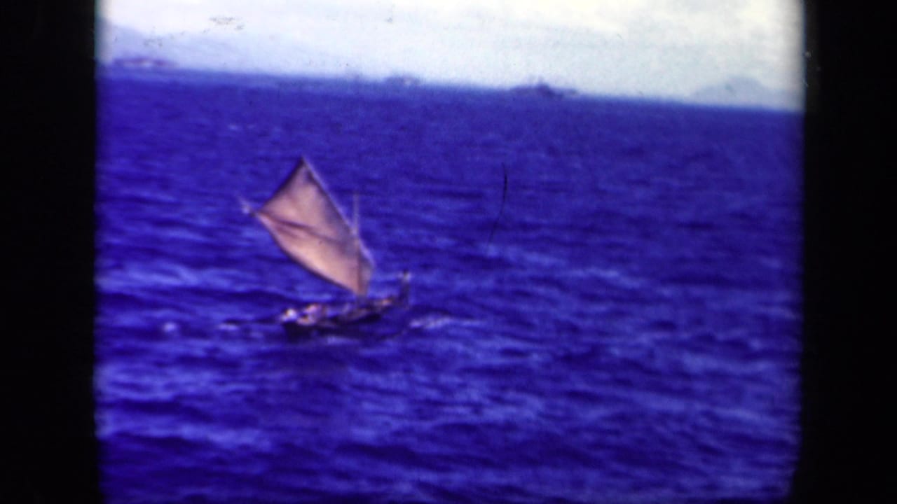1944 Leyte Gulf 8mm frame showing a distant small sailboat with a tan triangular sail crossing choppy blue water.