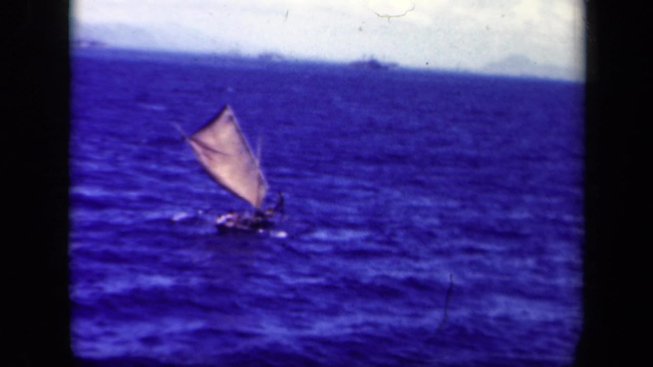 1944 Leyte Gulf home-movie frame with a small sailing vessel on rough blue water and faint landforms at the horizon.