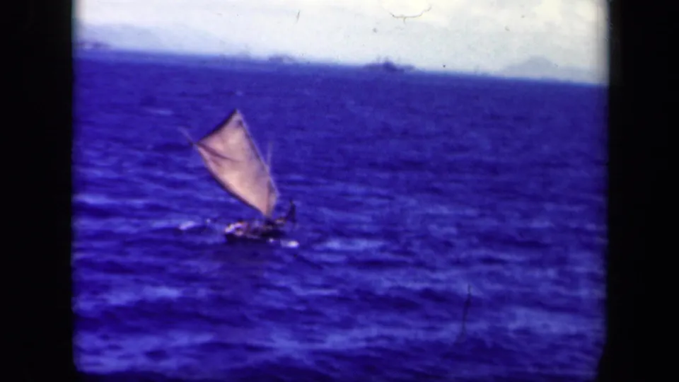 1944 Leyte Gulf home-movie frame with a small sailing vessel on rough blue water and faint landforms at the horizon.