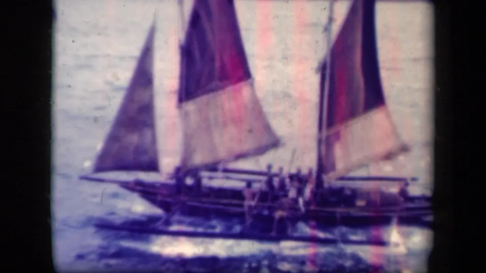 Closer 1944 Leyte Gulf view of a larger open sailboat with several people aboard and multiple canvas sails.