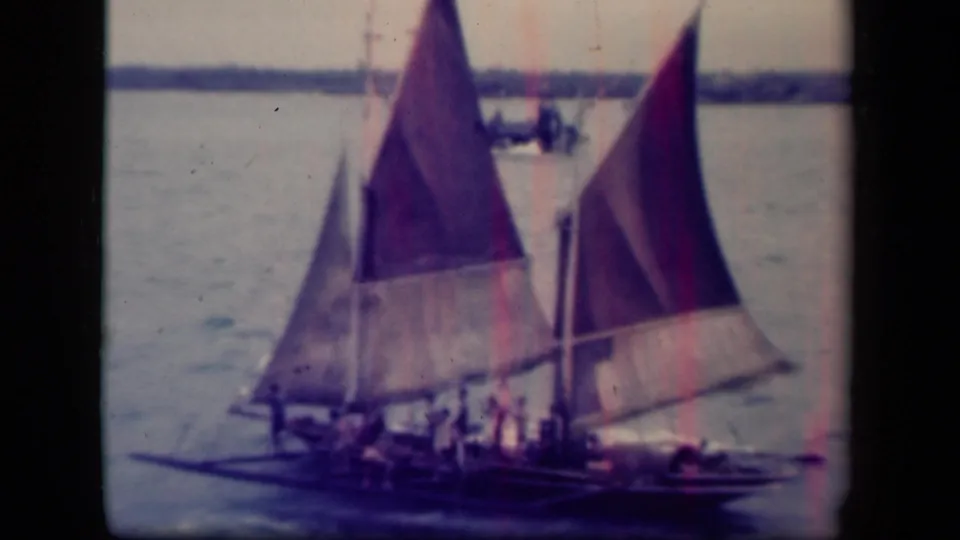 Two prominent traditional sailboats cross Leyte Gulf, their raised sails and small crew figures visible in soft 8mm color.