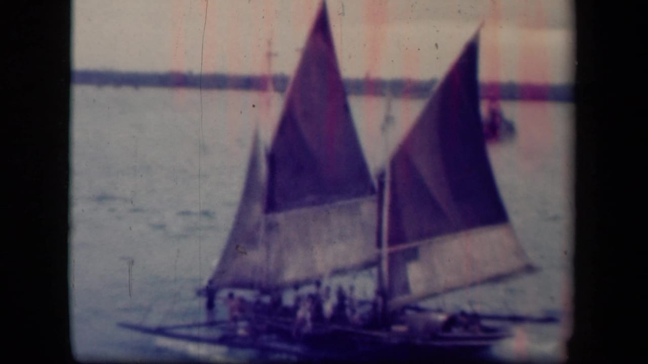 Sailing vessel with two raised sails and people aboard near a distant shoreline.